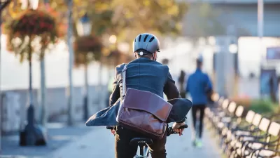 Rear view of man riding electric bike wearing business suit with large leather messenger bag slung across his back