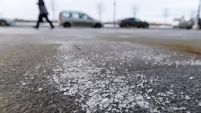 Low close-up of salt sprinkled on asphalt road in winter with person walking and car in background.