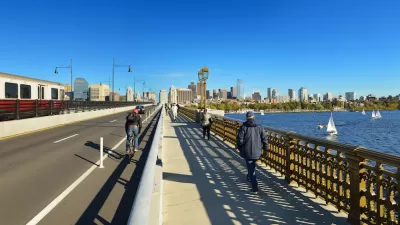 View of Boston skyline from Longfellow Bridge with cyclist riding in bike lane and pedestrian on sidewalk.