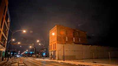 View of Chicago street with vacant lot and brick building, snow on the ground, at night.