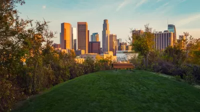 View of downtown Los Angeles at golden hour from top of grassy hill with wooden bench in Vista Hermosa Natural Park