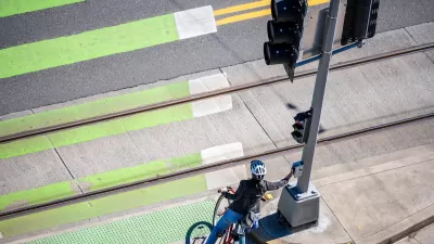 Cyclist pressing crossing button at green painted crosswalk.