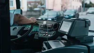 CLose-up of bus driver from behind with only hand on steering wheel visible.