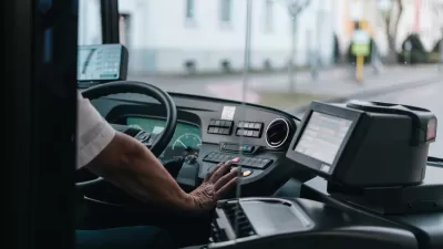 Close-up of bus driver from behind with only hand visible on steering wheel.