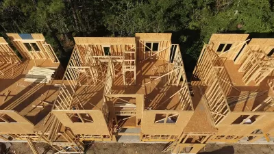 View from above of wood-frame multifamily housing under construction next to green trees.