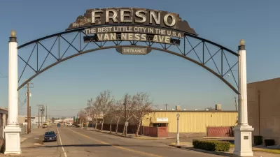 View of wide, deserted-looking street with arched sign reading "Fresno - Best little city in the U.S.A. - Van Ness Avenue - Entrance" in Fresno, California.
