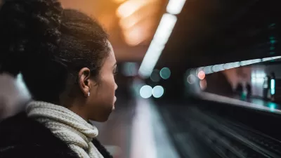 Close-up of woman waiting on fairly empty subway platform with tracks and opposing platform blurred in the background.