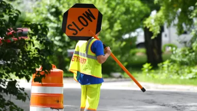 Worker in yellow safety suit holding up orange SLOW sign on road