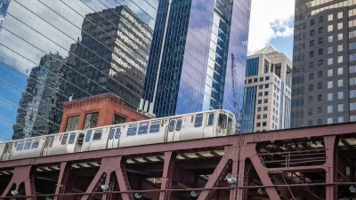 View up at Chicago elevated train line with train passing and glass high-rises in background.