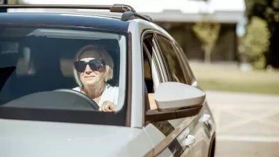 Senior woman wearing sunglasses sitting in the driver's seat of a silver car.