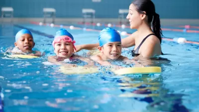 Female Coach In Water Giving Group Of Children Swimming Lesson In Indoor Pool.