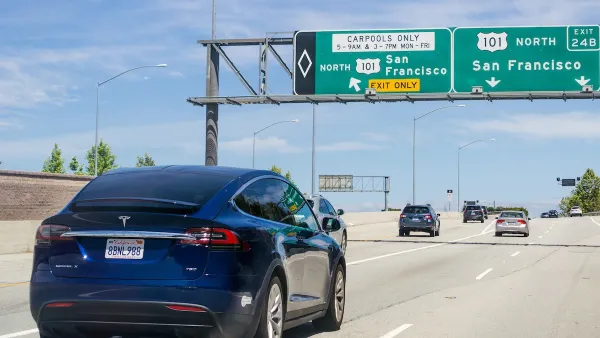 Dark blue Tesla sedan driving on freeway with green signs for San Francisco.