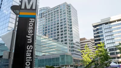 Close-up of Metro sign column at Rosslyn Station in Alexandria, Virginia with high-rose glass buildings in background.