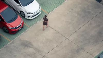 High view of woman walking in parking lot with red and white cars visible at left.