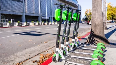 Several Lime e-scooters lined up next to curb on a sidewalk in San Jose, California.