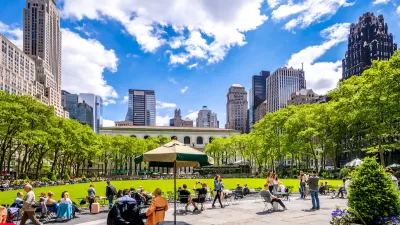 People sitting on lawn chairs in front of green meadow with New York City skyscrapers in background in Bryant Park, New York.