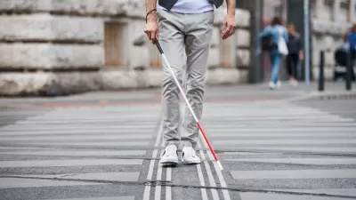 Low view of person with vision impairment cane walking through crosswalk.