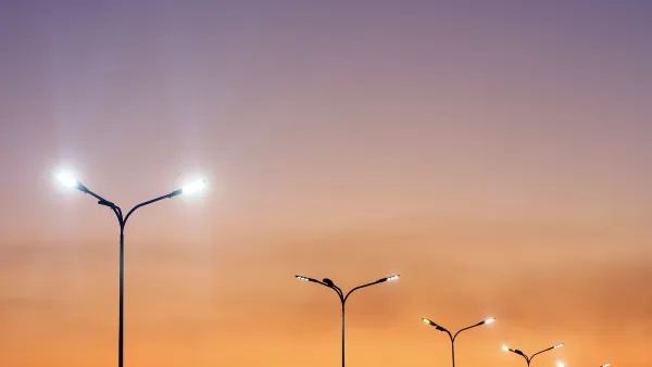 Row of double-headed street lights against orange sunset sky.