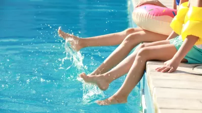 Close-up of two children sitting on edge of swimming pool with their feet in the water.