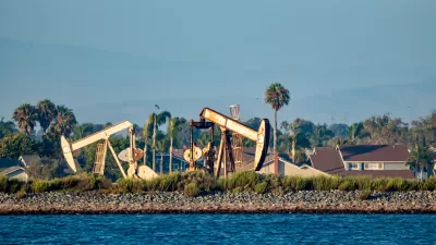 Oil drilling pumps on a wetland beach in California with houses in background