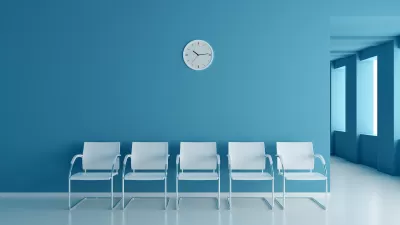 Row of five white chairs set against a blue wall with a round white analog clock. Clinic waiting room.