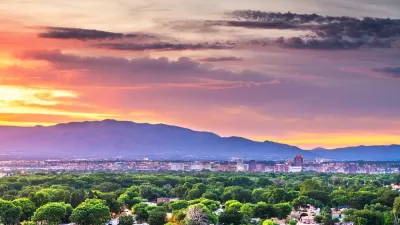 View of Albuquerque, New Mexico with green trees in foreground, mountains in background against sunset sky.