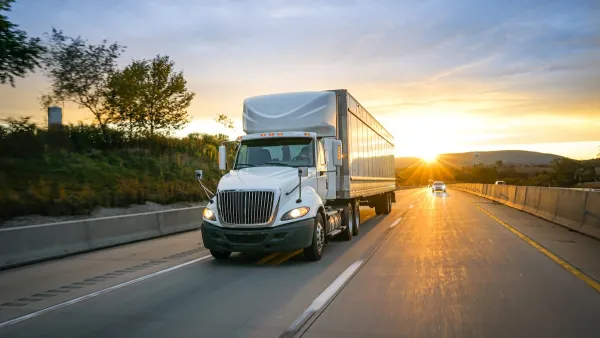 White freight truck on asphalt highway with sunset in background.