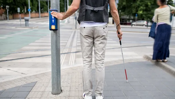 Pedestrian holding visual impairment cane pressing crosswalk button.