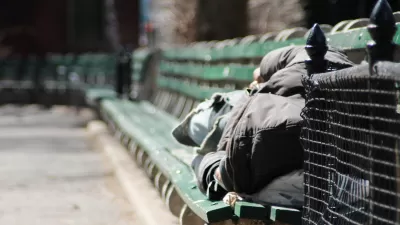 Person in black hoodie sleeping on green park bench in New York City park