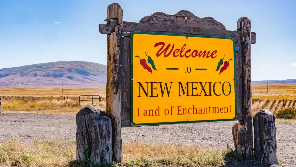 "Welcome to New Mexico - Land of Enchantment"  roadside sign with red text onyellow background and rustic wood frame around sign.
