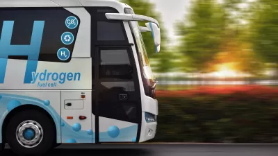 Side view of white bus with blue hydrogen fuel logo driving down the street.