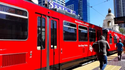 Red San Diego Trolley light rail train at station with passengers walking on platform and Spanish-style dome building in background.