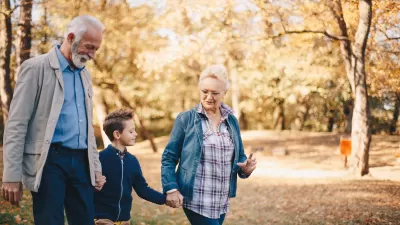Grandparents walking with young grandchild through park with fall foliage.