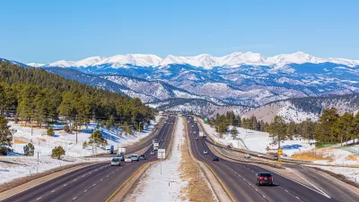 View of Colorado highway with light traffic and snowy Rocky Mountains in background.