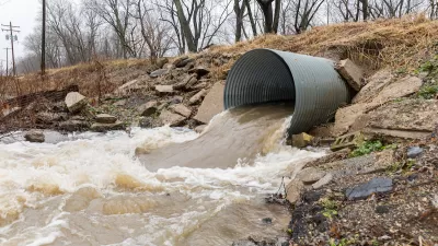 Large water pipe with brown water pouring out into dirt ditch.