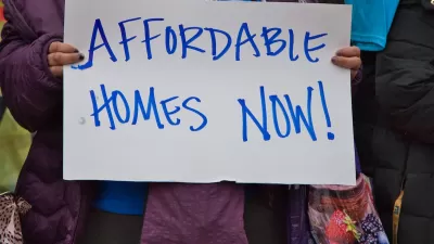 Close-up of person holding hand-written "Affordable Homes Now!" sign.