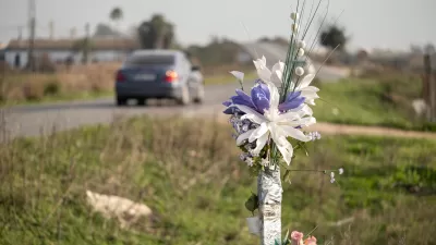 A bouquet of flowers stands in the grass beside a rural road as a car drives by.