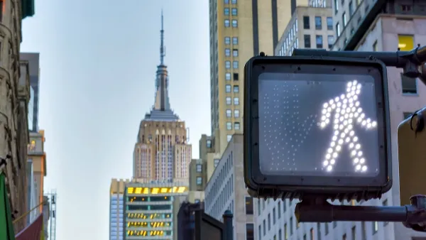 Close-up on pedestrian traffic signal with walk symbol lit up and Empire State Building spire visible in background.