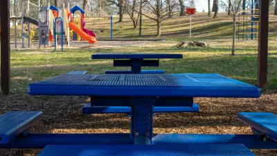 Blue picnic table with attached benches and colorful children's playground in background.