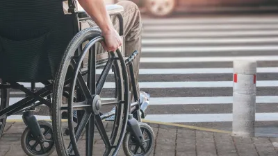 Close-up of man in manually operated wheelchair waiting at urban crosswalk.