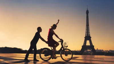 Silhouette of man holding on to back of bicycle ridden by woman with Eiffel Tower in background.