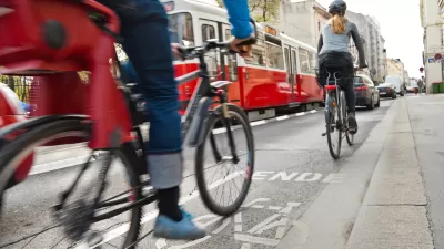 Cyclists in bike lane with red streetcar in background on urban street.