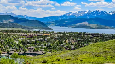 Scenic overlook of town with a lake and snowcapped mountains in the background.