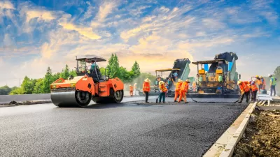 Crew in orange safety vests stand on roadway next to orange heavy equipment