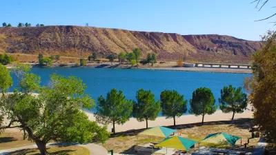 A view of a recreational area in front of a bright blue Castaic Lake in LA County with arid flat hills in the background.