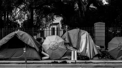 Black and white photo of row of tents set up against fence outdoors.
