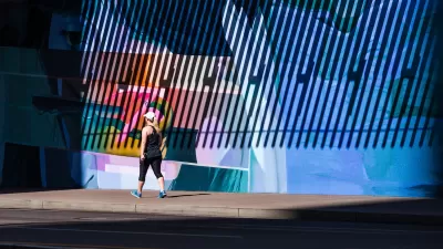 Woman in exercise clothes walking on sidewalk against large wall with mural in Phoenix, Arizona.