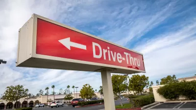 Close-up of red sign with white "Drive-Thru" text and arrow pointing left against partly cloudy blue sky.