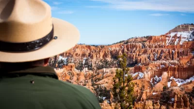 Close-up of park ranger in green jacket and khaki hat looking out at Bryce Canyon National Park red rock formations.