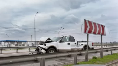 White truck with crumpled front sitting on highway after crash.
